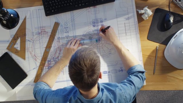 Top View of a Technical Engineer Working on His Blueprints, Drawing on Plans. Various Drawing Objects Lying on his Table.  Shot on RED Cinema Camera in 4K (UHD).