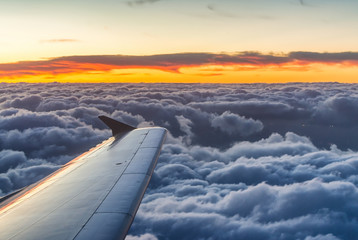 Fototapeta na wymiar Airplane wing at sunset over sky clouds