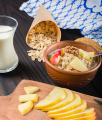 Cooked porridge oatmeal in a bowl on wooden dark background. Ingredients for cooking.