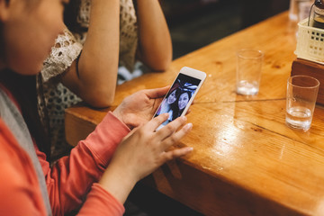 Two japanese female friends at the restaurant while waiting for their dishes taking selfies with smartphone