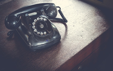 Black antique vintage analog telephone dialing or scrolling phone on wooden table. Contact us...