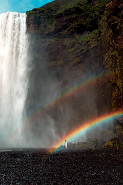 Woman standing underneath rainbow and waterfall