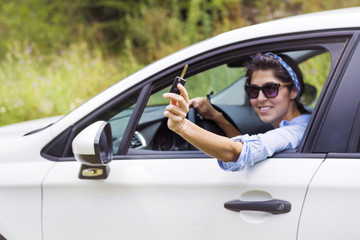 Young happy woman driving new white car with keys in the hand
