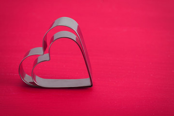 Valentine background with two metal hearts on pink wood.
