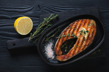 Frying pan with grilled salmon steak over black wooden surface
