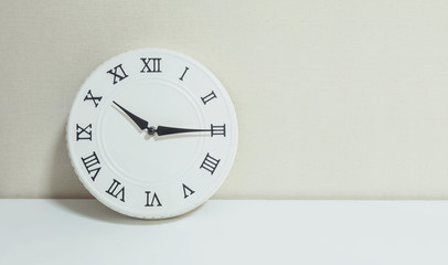 Closeup white clock for decorate show a quarter past ten or 10:15 a.m. on white wood desk and cream wallpaper textured background with copy space