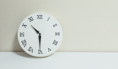 Closeup white clock for decorate show half past ten or 10:30 a.m. on white wood desk and cream wallpaper textured background with copy space