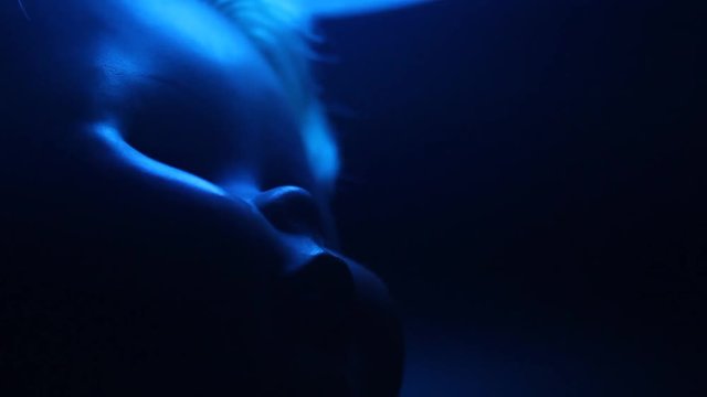 Horror video of a plastic close-up doll face under blue swinging lamp light.