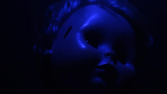Horror video of a plastic doll under blue lamp with thick blood dripping on a face.