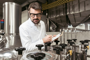 Concentrated man noting work results on beer factory