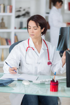 woman doctor analyzing x ray of patient and taking notes