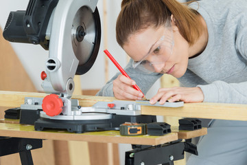 Female worker marking where to cut wood with circular saw
