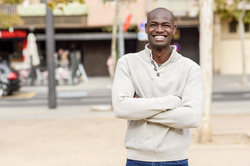 Black young man with arms crossed smiling in urban background