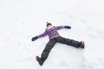 Fototapeta na wymiar Little girl in winter pink hat in snow forest doing an angel