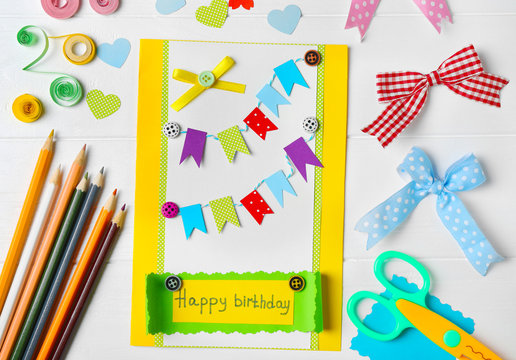 Handmade gift card and colorful crayons on white wooden background