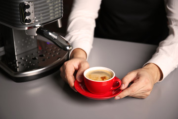 Male barista holding red cup of coffee at table