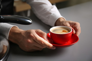 Fototapeta na wymiar Male barista holding red cup of coffee at table