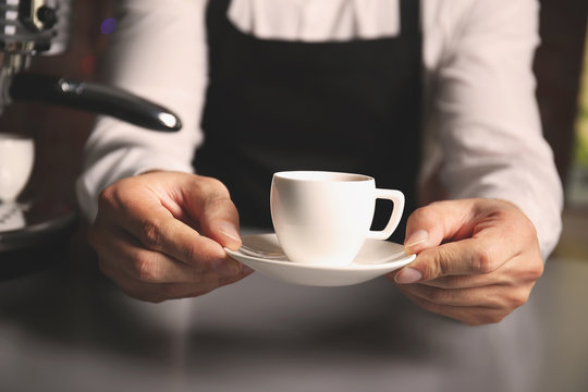 Male barista holding cup of coffee at table