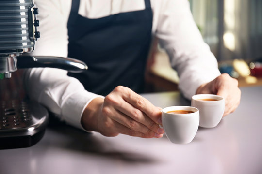 Male barista holding two cups of coffee at table