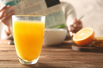 Glass of juice and tasty breakfast on table with person reading newspaper on background