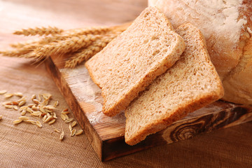 Sliced bread with wheat spikes on wooden table closeup