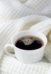 White cup with hot coffee wrapped in a white woolen scarf