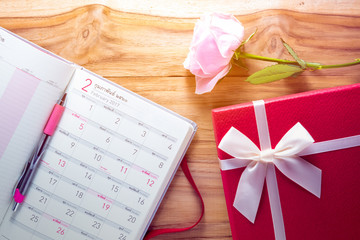 Gigt box with calendar book , rose flower and white ribbon. Valentines day simbols on a wood background