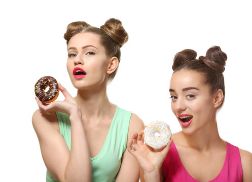 Funny young women with tasty donuts on white background