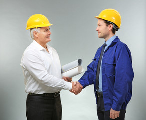 Senior engineer and worker shaking hands on light background
