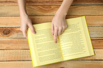 Naklejka premium Female hands holding opened book on wooden background
