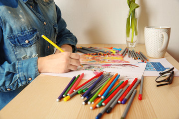 Young woman sitting at table with coloring pictures for adults, closeup