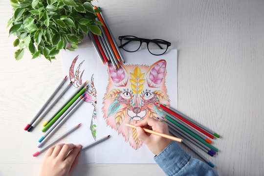 Young woman sitting at table with coloring pictures for adults, closeup