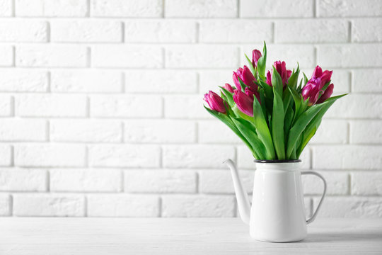 Vase with bouquet of beautiful tulips on brick wall background