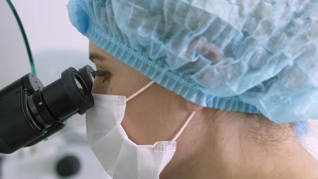 Two women scientists in disposable caps and masks looking through microscopes
