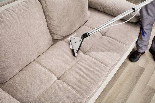 Person Cleaning Sofa With Vacuum Cleaner