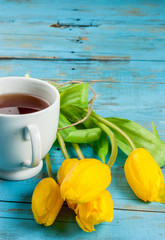 Spring flowers tulips and cup of tea on a light blue rustic wooden table, copy space, vertical
