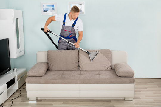 Male Worker Cleaning Sofa With Vacuum Cleaner