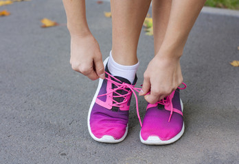 Naklejka premium Woman tying shoelace on running shoes before practice. Bright running shoes. Fitness woman in training shoes jogging outdoors in park. 