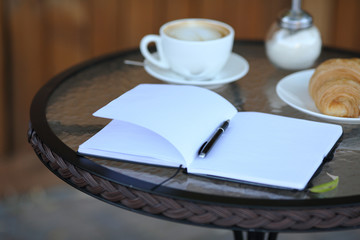 Diary on the table with coffee and croissant