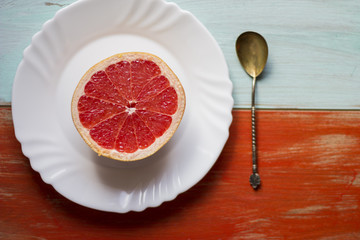 an orange with the shape of a coffee cup and a grey fruit with the shape of a heart in the center of it together with an old silver teaspoon and a plate on a light blue and orange wooden background.