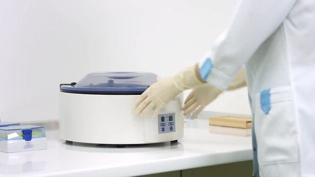 Embryologist put test tube with sperm sample into Laboratory centrifuge, close lid and press start button, scientist work in lab.