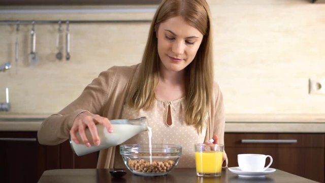 Beautiful young attractive woman pouring milk into a bowl of cornflakes in the kitchen.