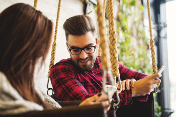 Young hipsters swinging and man is watching photos on his girlfriend smartphone.
