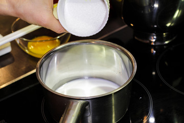 Adding white sugar into a sauce pan filled with milk