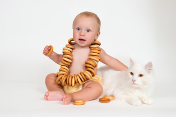 Funny baby sits with bunch of bagels and hugging a cat on white background.