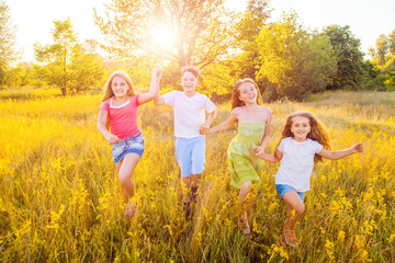 Fototapeta premium four happy beautiful children running playing moving together in the beautiful summer day. jumping and looking at camera with happiness and toothy smile. 