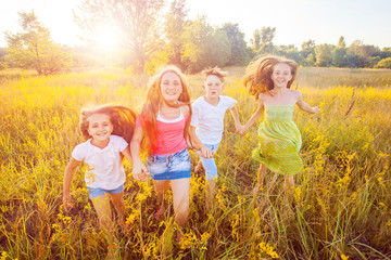 four happy beautiful children running playing moving together in the beautiful summer day. jumping and looking at camera with happiness and toothy smile. 
