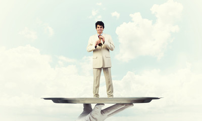 Businessman on metal tray playing fife against blue sky background