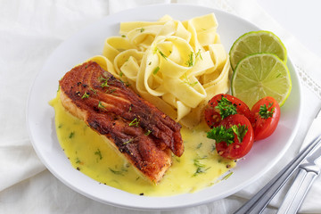 Grilled salmon dish with lemon sauce and tagliatelle pastaon a white tablecloth