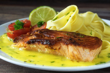 Grilled salmon with lemon sauce and tagliatelle pasta on dark wood, close up